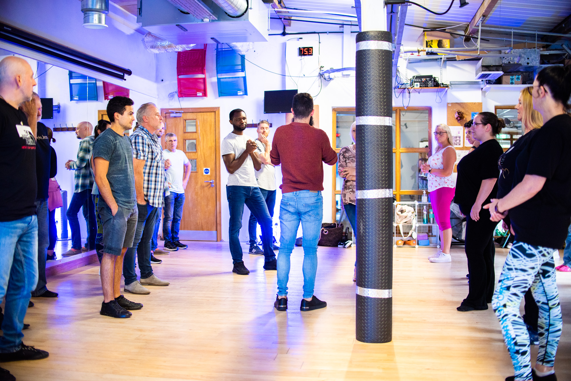 Workshop group in a circle in a bright studio, bearded instructor in a red jumper teaching
