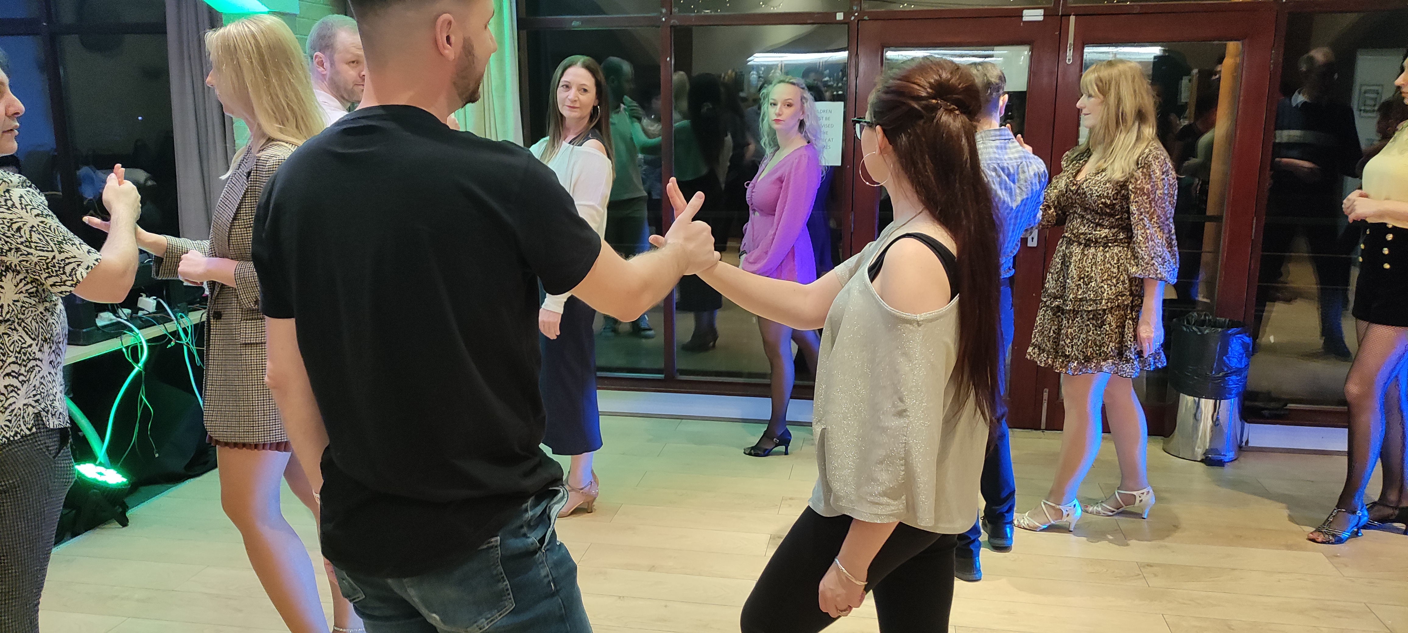 Dancers mid-move, a couple in the foreground sharing a thumbs-up hand connection