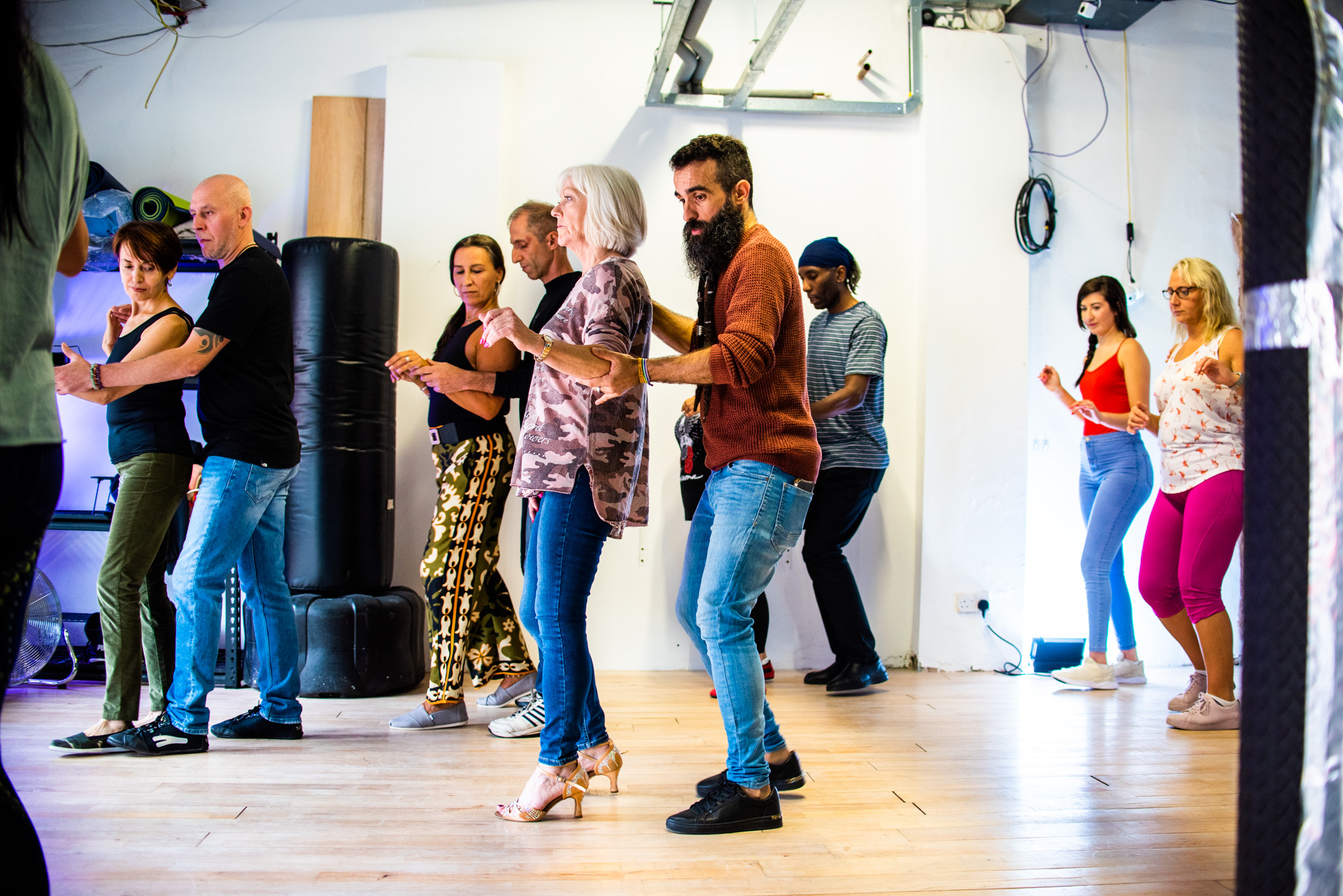 A line of students practising footwork and hold in the bright studio