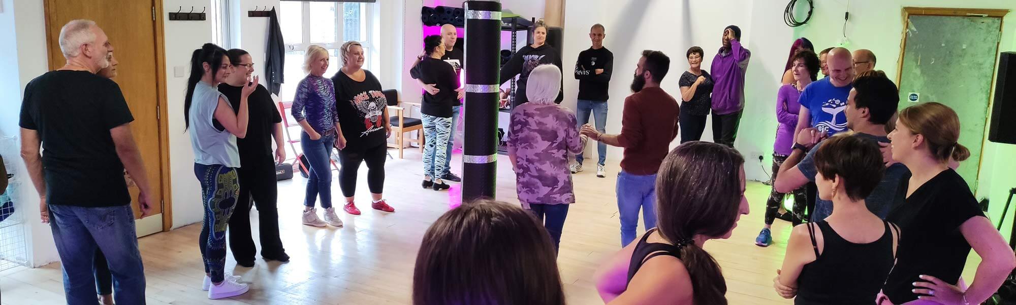 A Salsa Belfast class in a bright studio, the group standing in a circle around a pillar as the instructor demonstrates